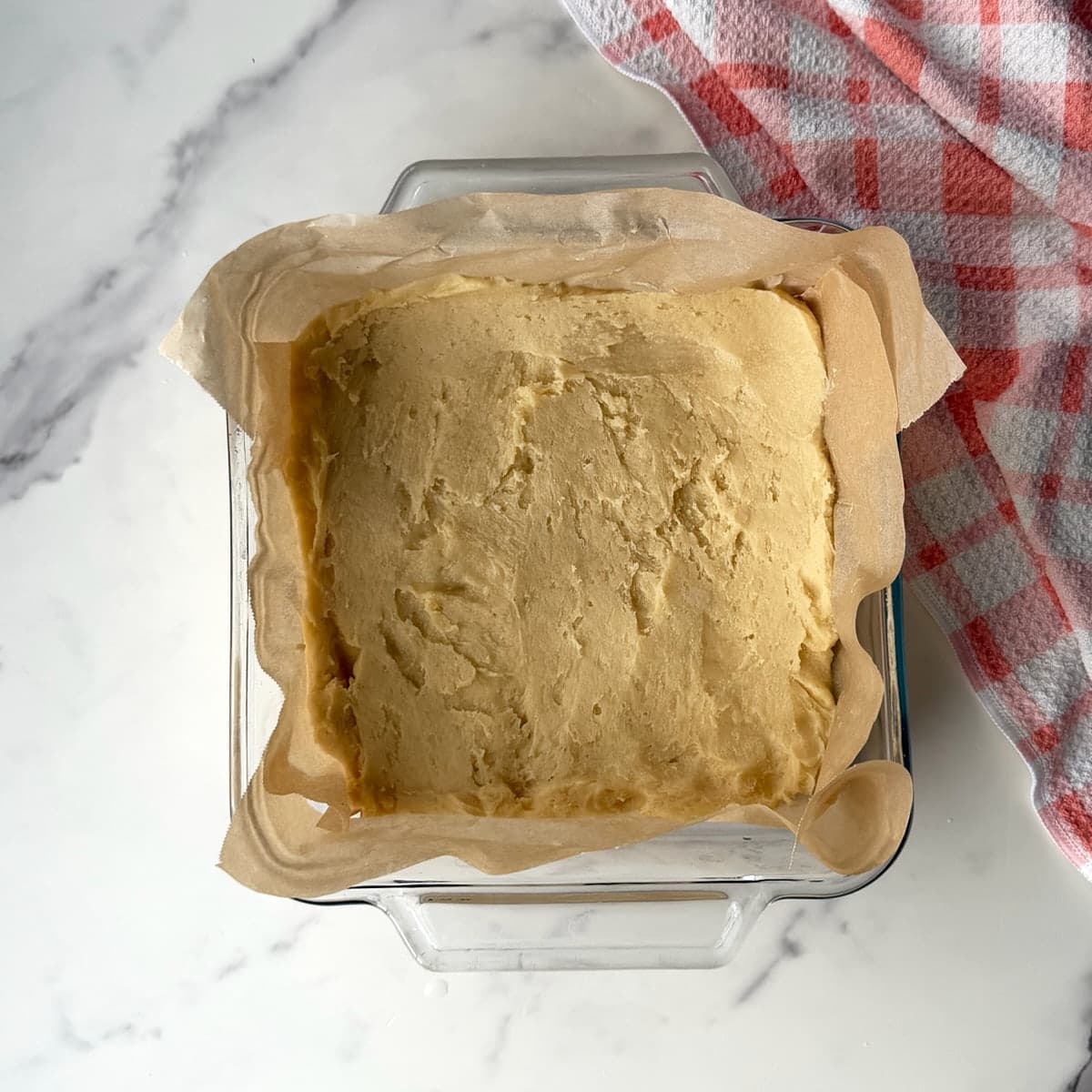 sourdough sugar cookie bar pressed into a glass 8x8 baking dish lined with parchment paper.