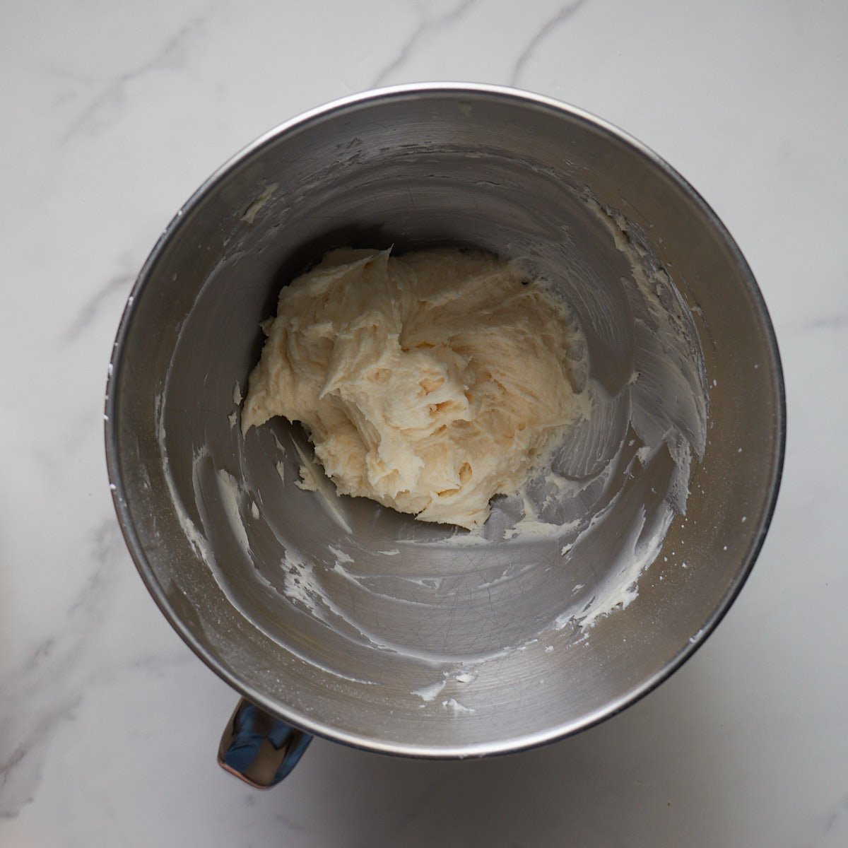 Frosting for the sourdough sugar cookie bars mixed in a metal kitchen aid bowl.