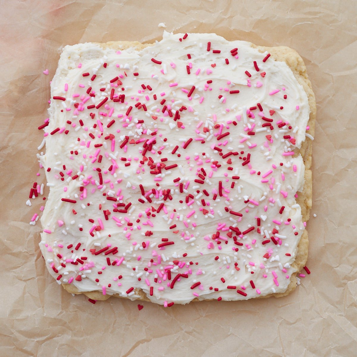 Sourdough discard sugar cookie bar with frosting and sprinkles on parchment paper.
