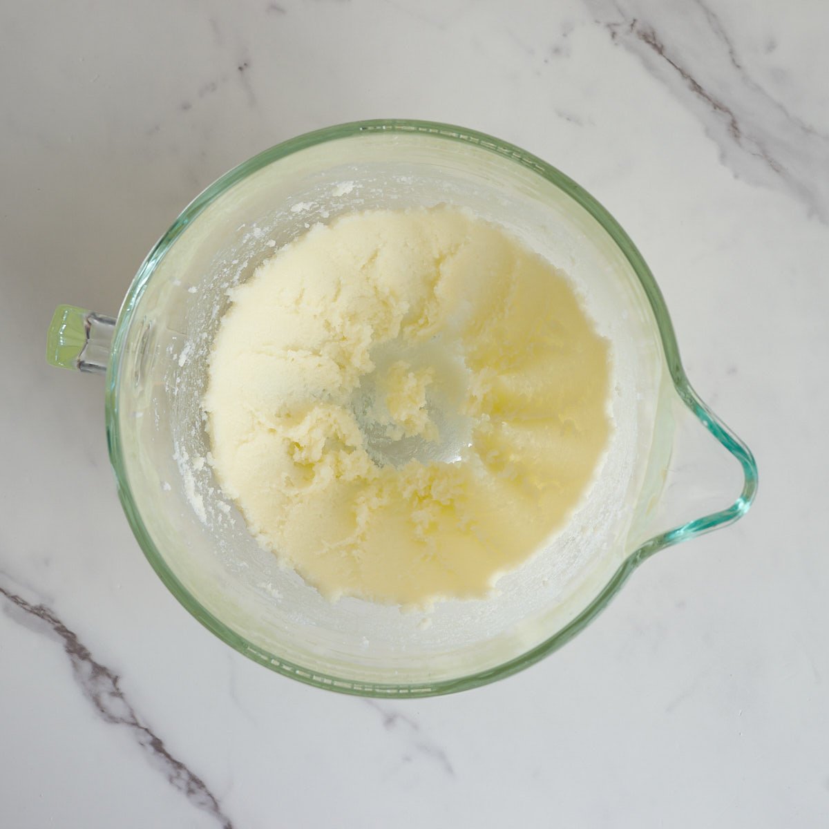Creamed butter and sugar in a large glass mixing bowl with a marble background.