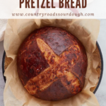 A pinterest pin of a top-down view of cheesy sourdough pretzel bread after baking resting on a sheet of parchment paper.