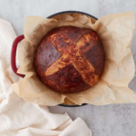 A pinterest pin of a top-down view of cheesy sourdough pretzel bread after baking resting on a sheet of parchment paper.