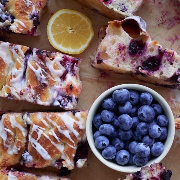 Lemon Blueberry Sourdough Focaccia sliced on parchment paper next to a bowl of blueberries and a lemon slice.