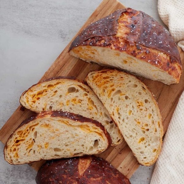 Cheesy sourdough pretzel bread sliced and arranged on a wooden cutting board.