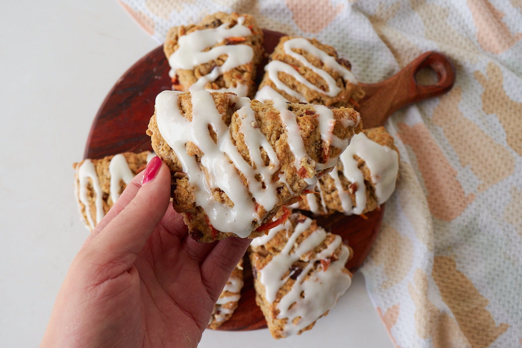 Hand holding a Sourdough Carrot Cake Scone with a drizzle of cream cheese frosting.