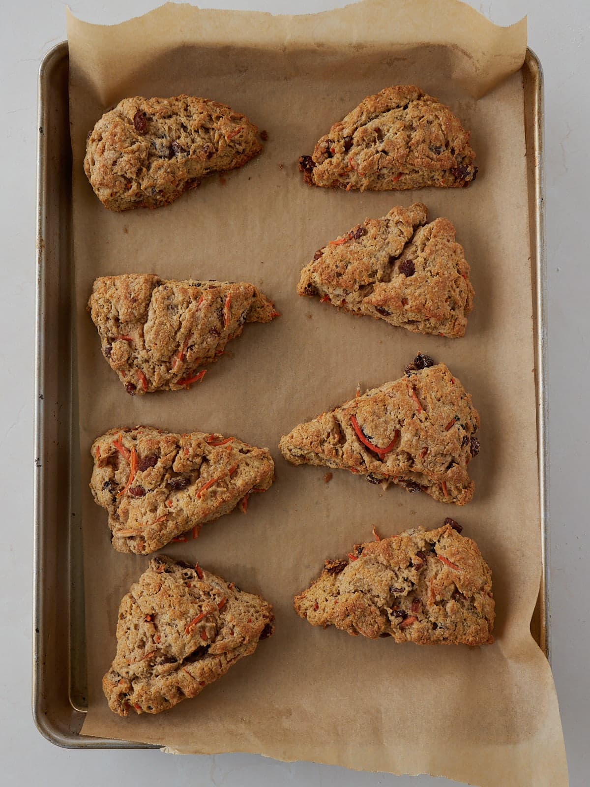 Freshly baked sourdough carrot cake scones on a parchment paper lined sheet pan.