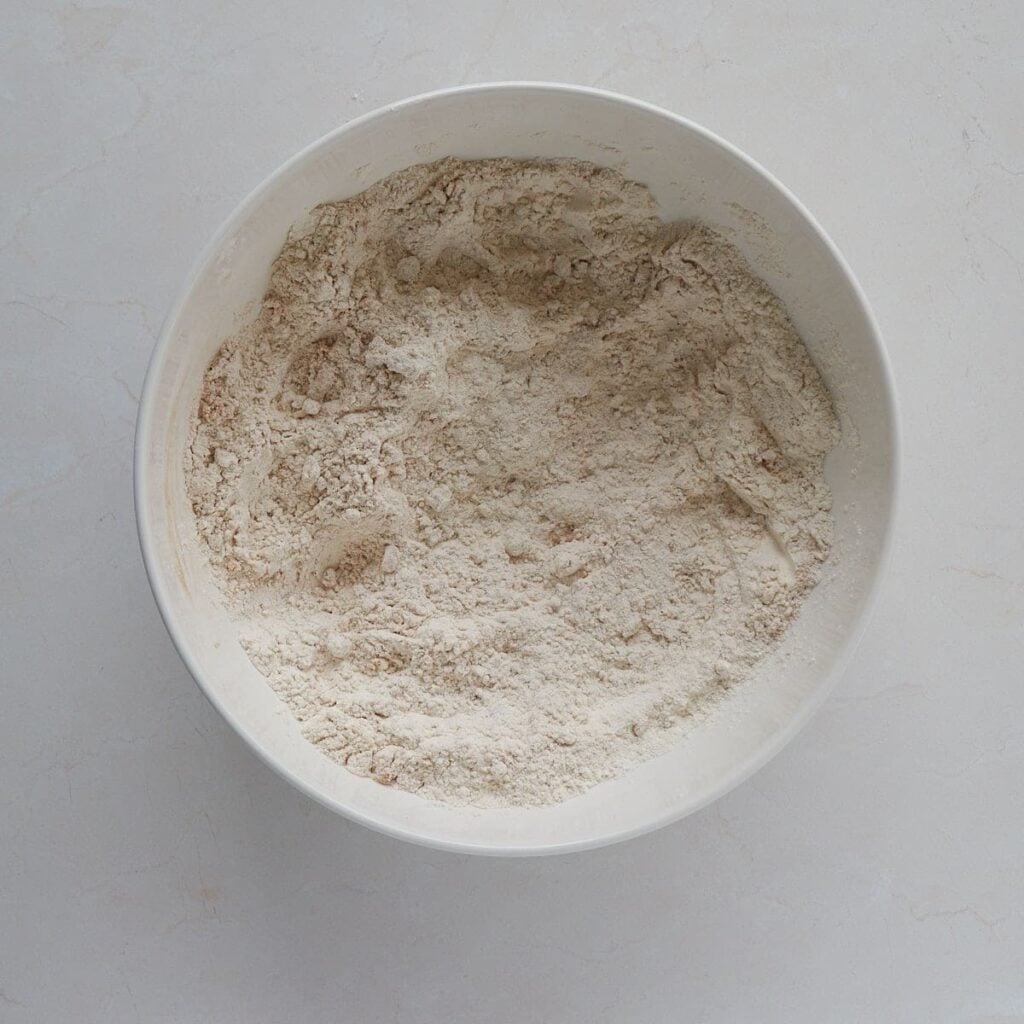 Dry ingredients for Sourdough Carrot Cake Scone in a white bowl.