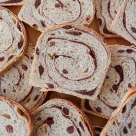 Slices of Sourdough Cinnamon Raisin Bread stacked on top of each other on a wooden background.