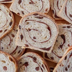 Slices of Sourdough Cinnamon Raisin Bread stacked on top of each other on a wooden background.