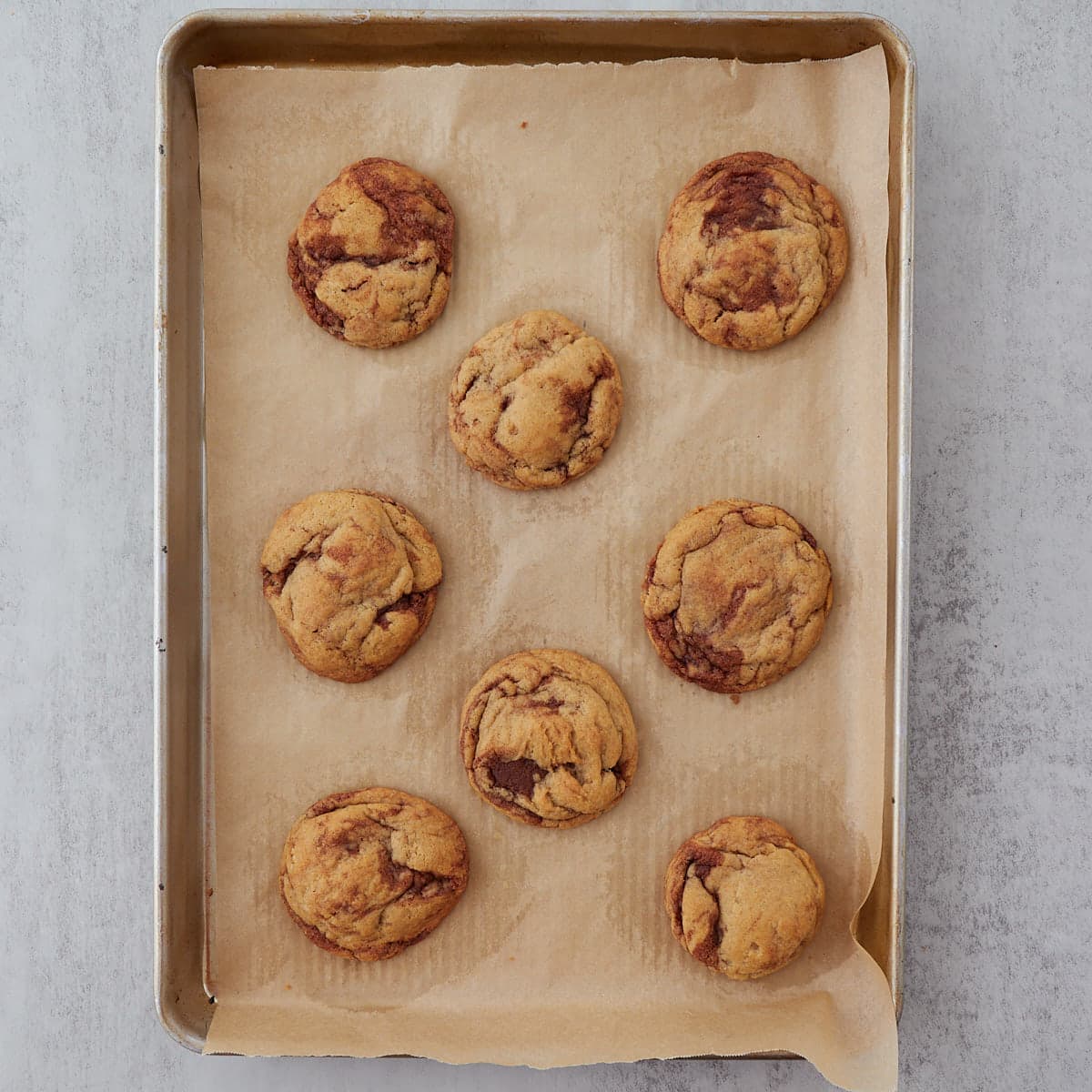 Eight sourdough cinnamon roll cookies on a parchment lined baking sheet after baking.