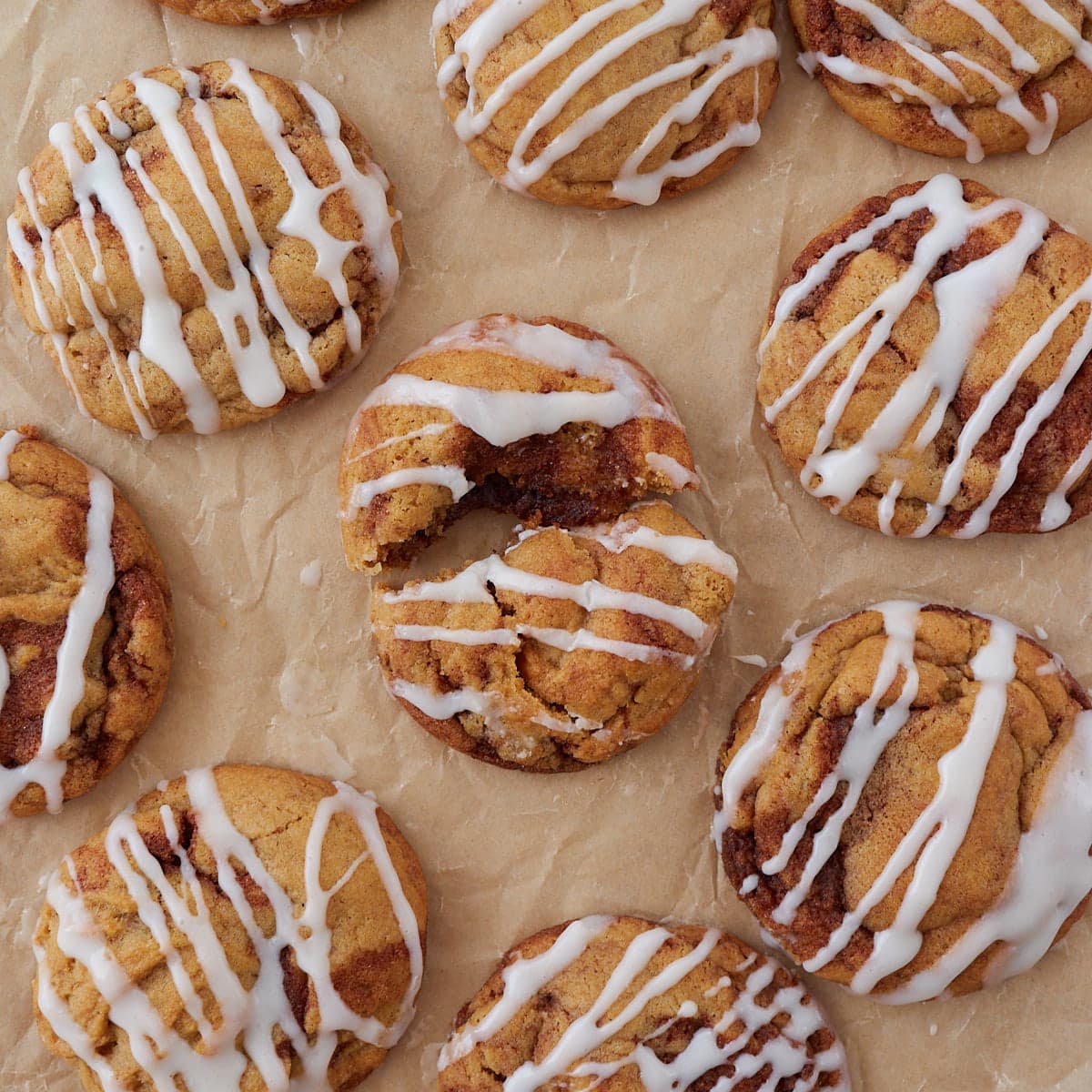 Sourdough cinnamon roll cookies with cream cheese icing arranged on parchment paper. One cookie is broken in half.