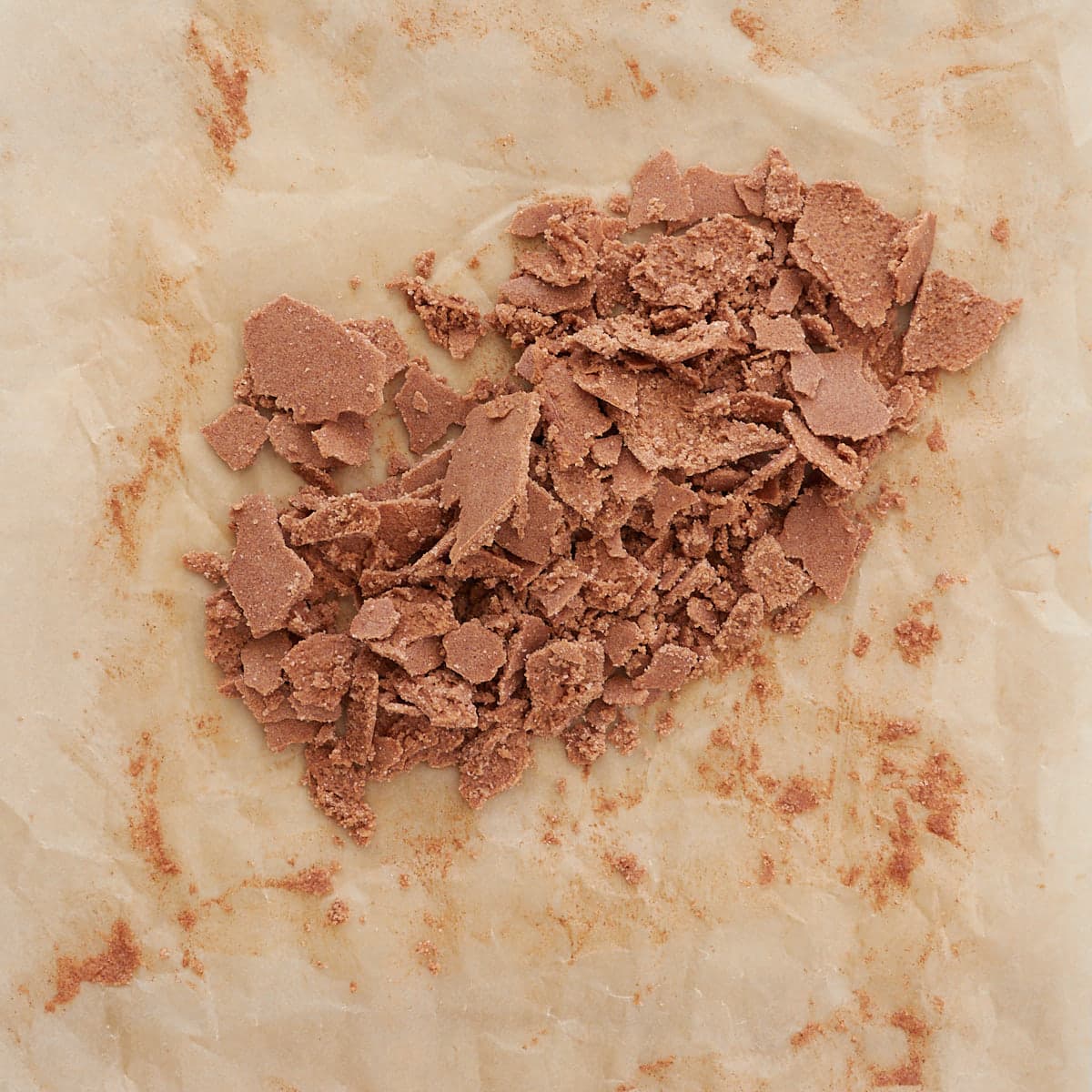 A thin layer of the brown sugar, butter, and cinnamon mixture for sourdough cinnamon roll cookies crumbled up on a piece of parchment paper after freezing.