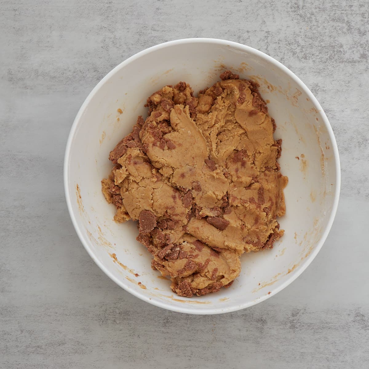 Cinnamon sugar pieces folded into the sourdough cinnamon roll dough until it's just incorporated in a large white mixing bowl.