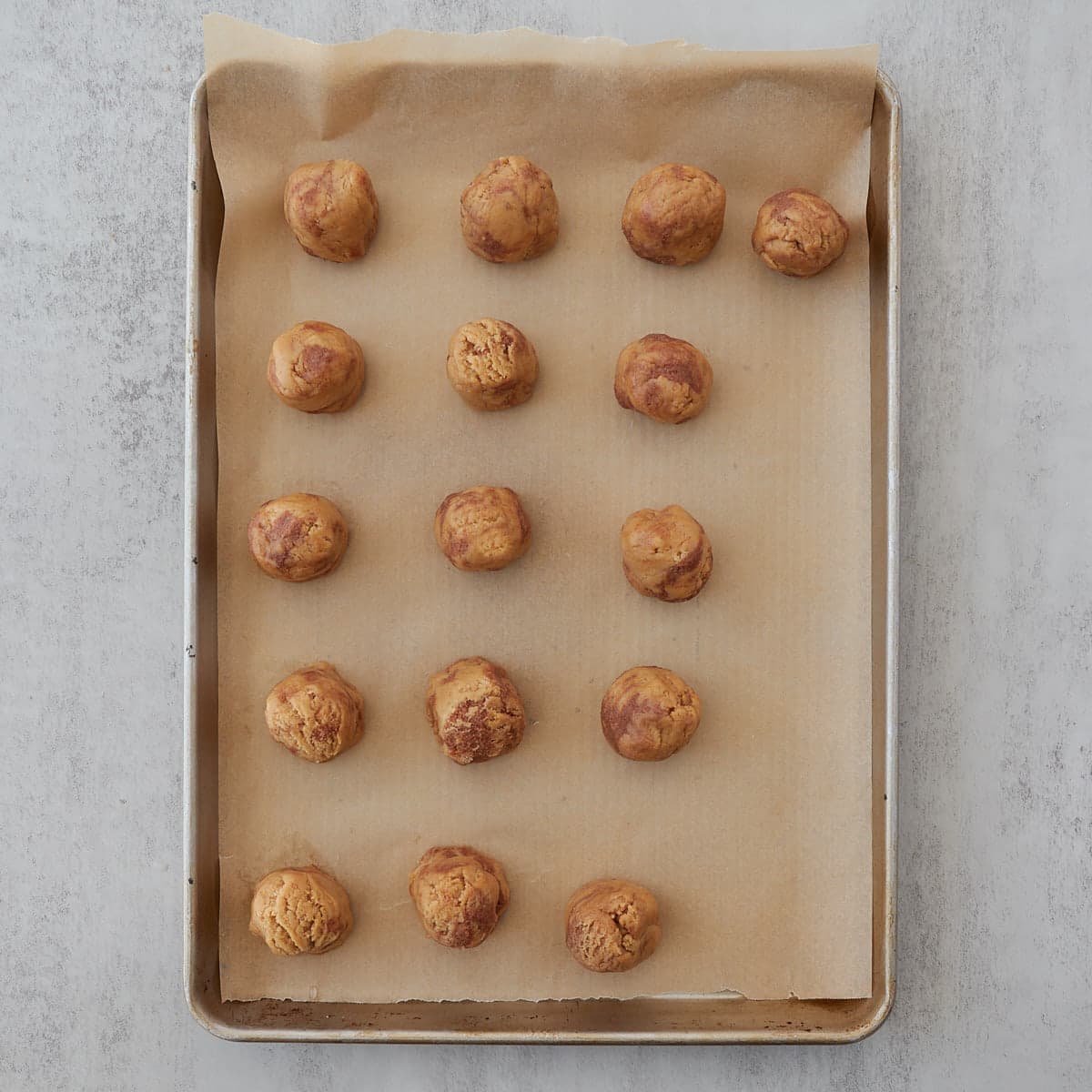 Sourdough cinnamon roll cookie dough balls on a parchment lined cookie sheet prepped to chill in the fridge.
