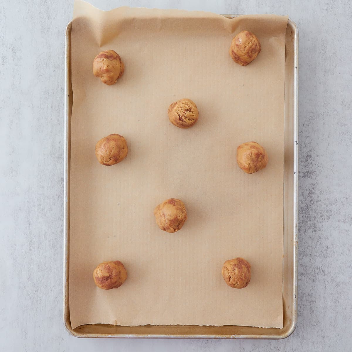Eight sourdough cinnamon roll cookie dough balls on a parchment lined cookie sheet after chill, ready to bake.