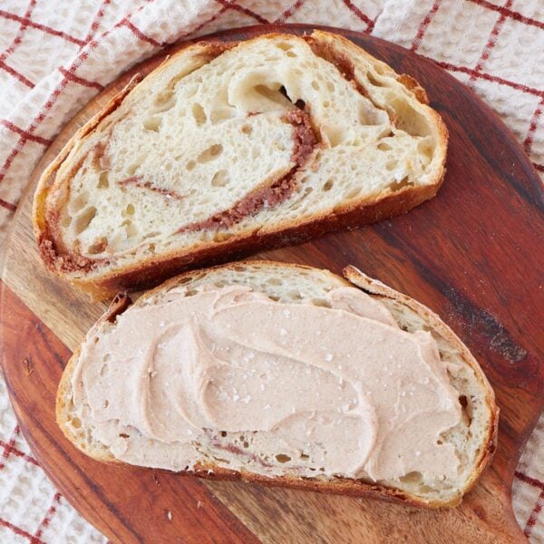 Cinnamon honey butter swirled into 2 slices of sourdough bread on a round wooden charcuterie board with more cinnamon honey butter spread on top of one slice.