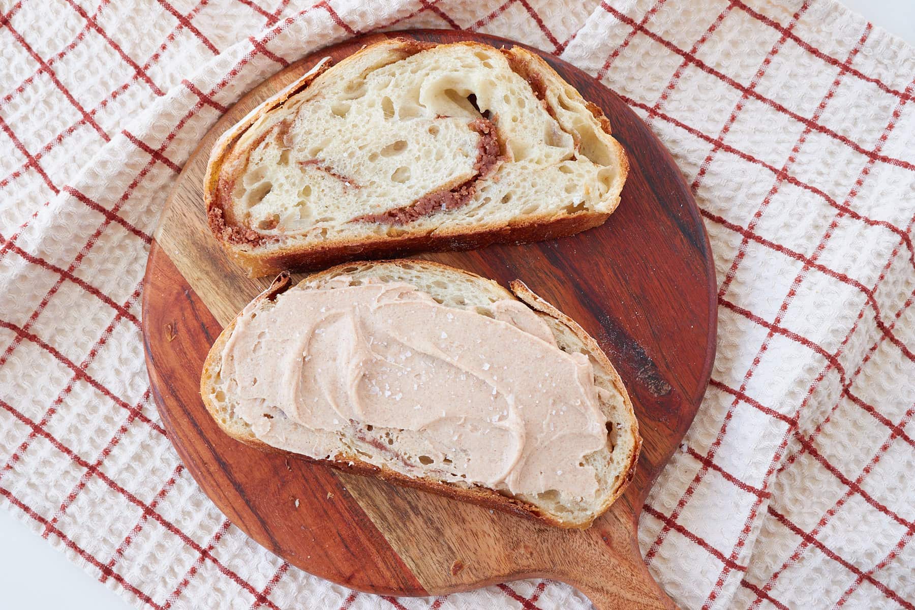 Cinnamon honey butter swirled into 2 slices of sourdough bread on a round wooden charcuterie board with more cinnamon honey butter spread on top of one slice.