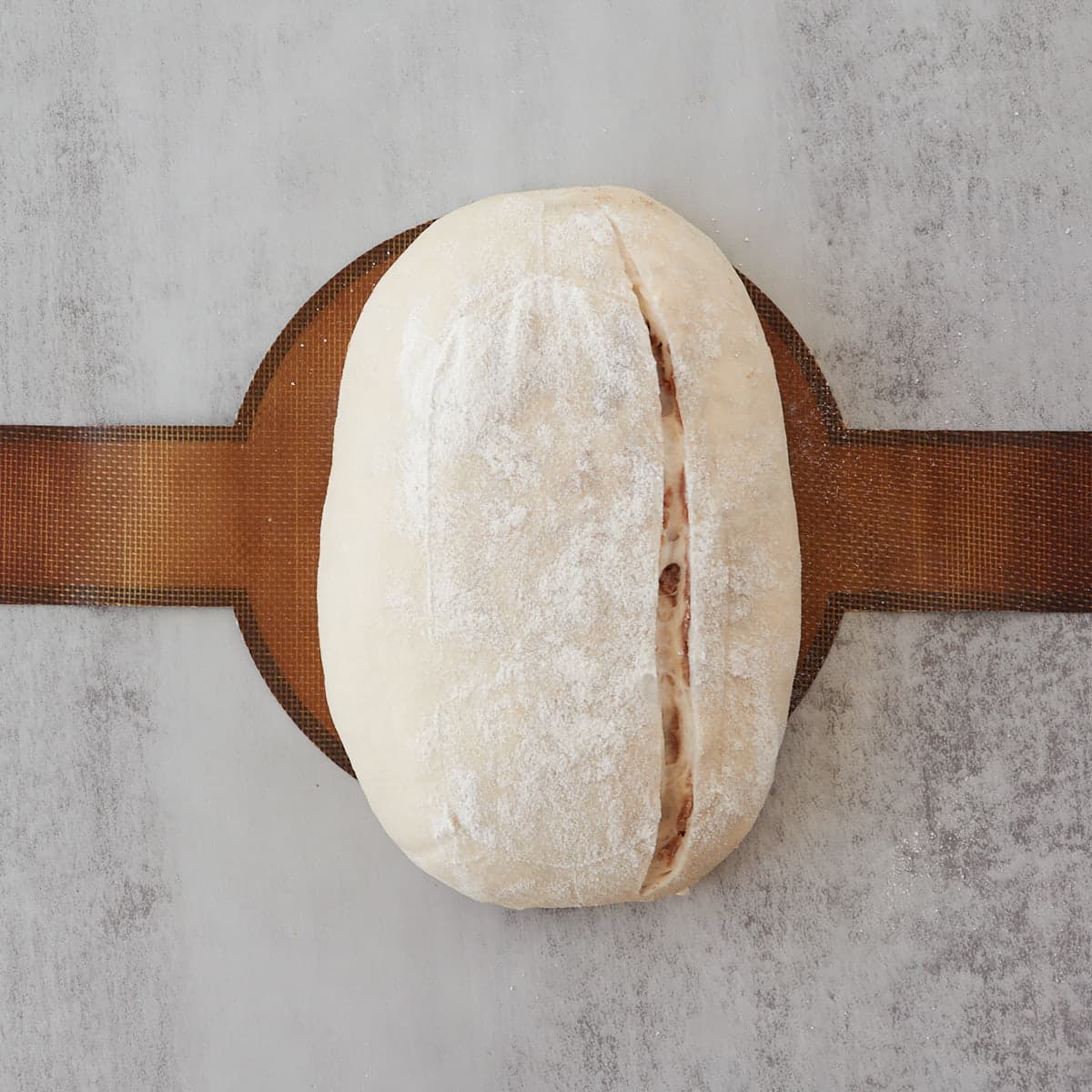 Oval sourdough bread dough with a large slash down the side on a silicone baking mat before baking.