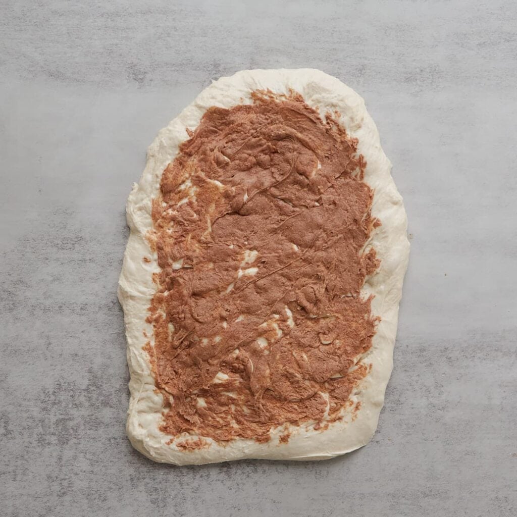 Cinnamon honey butter spread all over a stretched out sourdough bread dough.