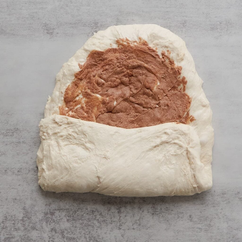 Sourdough bread dough with one side folded up halfway with cinnamon honey butter in the middle.