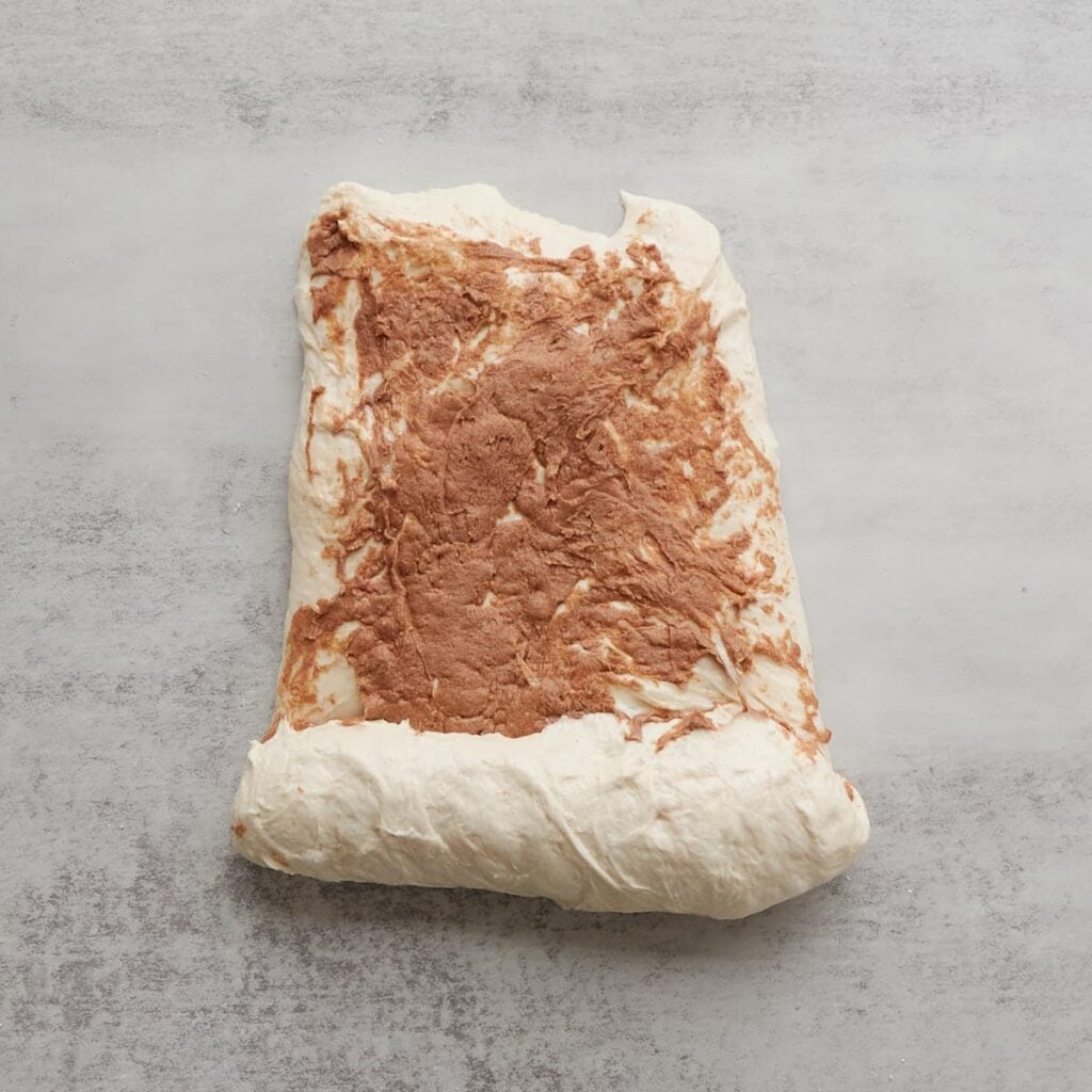 Cinnamon honey butter spread on a loaf of sourdough bread that is starting to be rolled up.