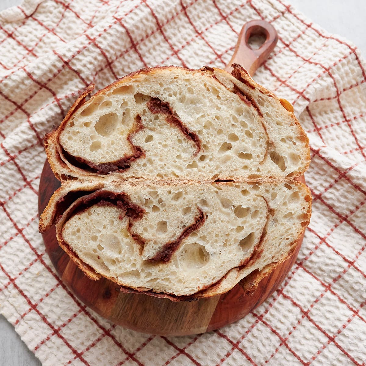 Sourdough Cinnamon honey butter bread swirled in a loaf that is cut in half on a round brown board.