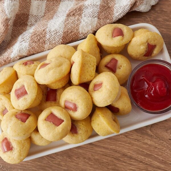 A white platter filled with Sourdough Mini Corn Dogs and a small bowl of ketchup.