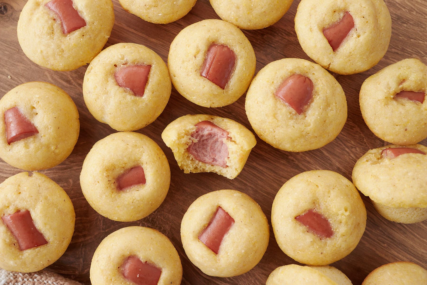 Sourdough Mini Corn Dogs on a wooden surface with one bite taken out of the mini corn dog in the center.