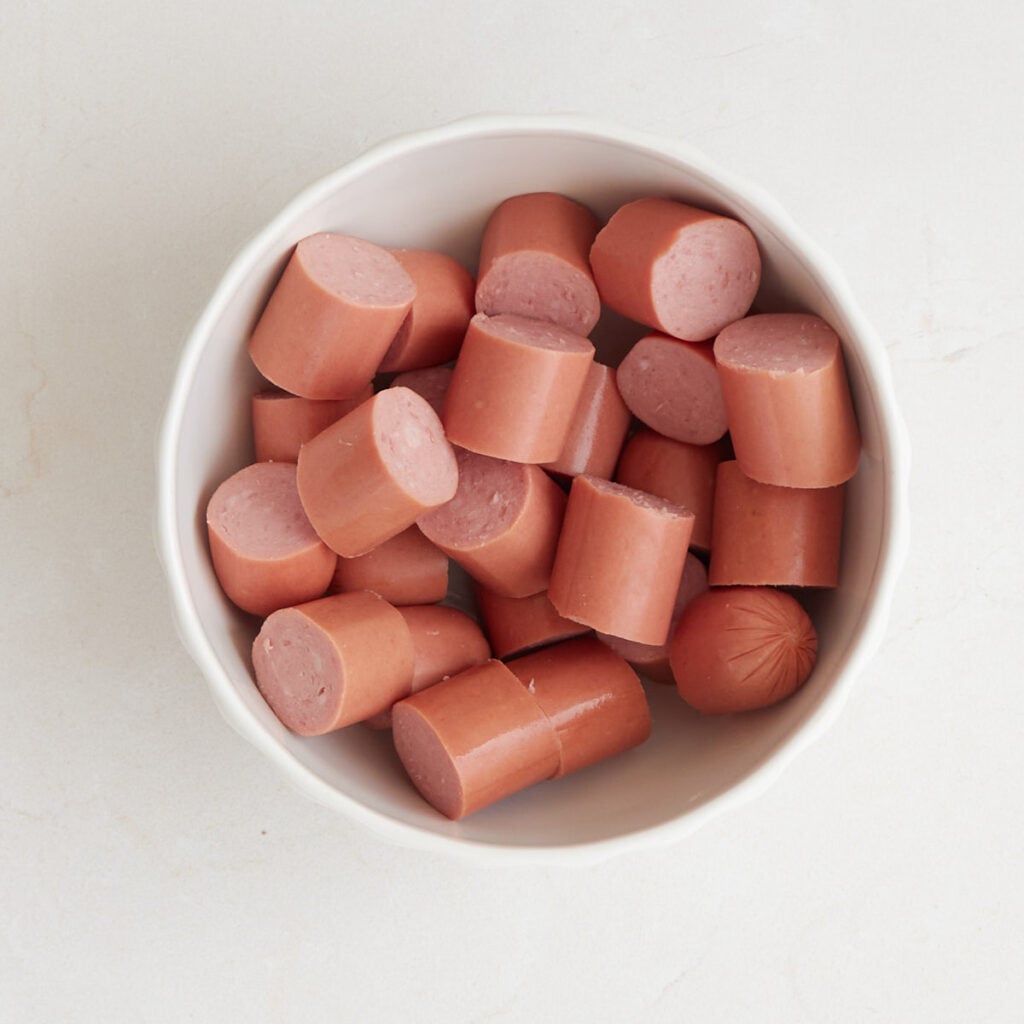 Hot dogs cut into small pieces in a white bowl.