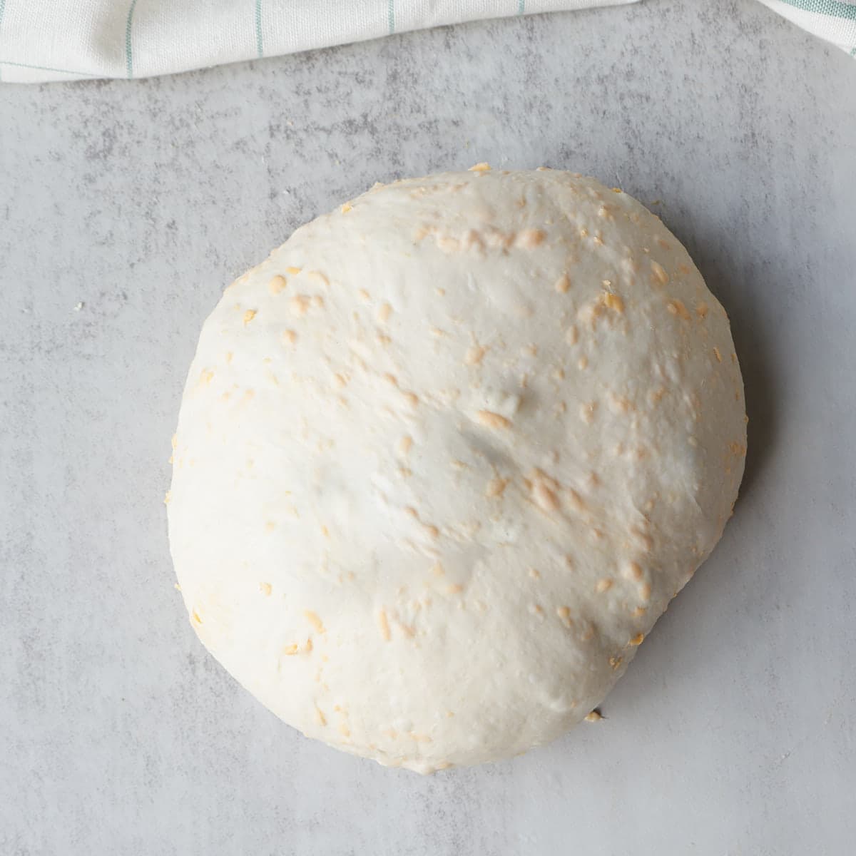 Cheesy sourdough pretzel bread dough shaped and resting on a marble counter.