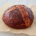 An angled photo of a loaf of Cheesy Sourdough Pretzel Bread on a piece of parchment paper set on a marble surface.