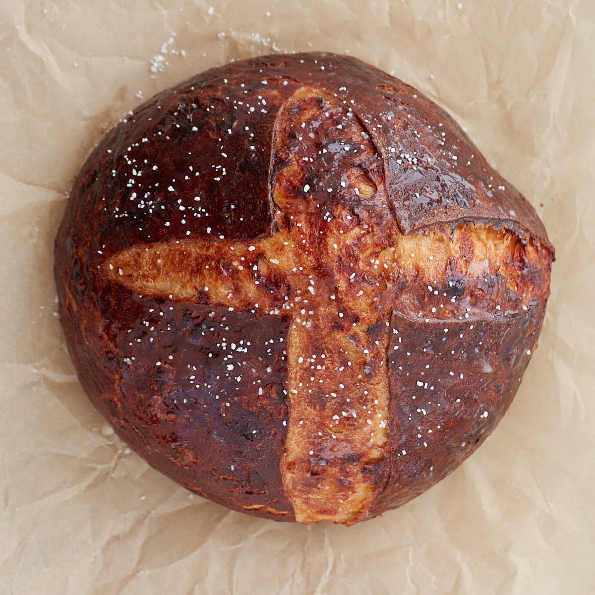 Top-down view of cheesy sourdough pretzel bread after baking resting on a sheet of parchment paper.