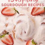 Pink cream cheese frosting on top of strawberry sourdough rolls with fresh slices of strawberries.