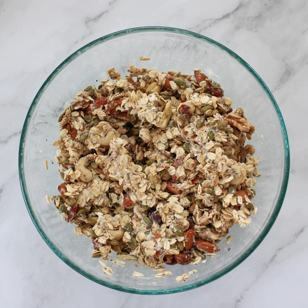 Wet ingredients added to dry ingredients for sourdough granola in a clear bowl.