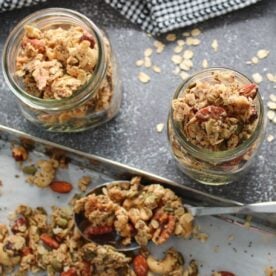 Sourdough Granola in mason jars next to a sheet pan and silver spoon filled with granola .