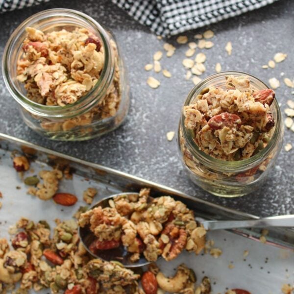 Sourdough Granola in mason jars next to a sheet pan and silver spoon filled with granola .