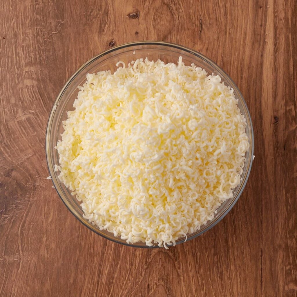 Butter shredded in a clear bowl on a wooden surface.
