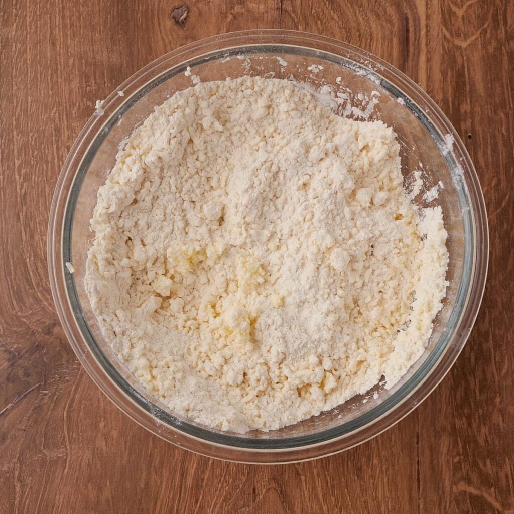 Butter mixed with dry ingredients in a clear bowl for sourdough buttermilk biscuits.