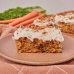 One slice of sourdough carrot cake with cream cheese frosting on a brown plate.