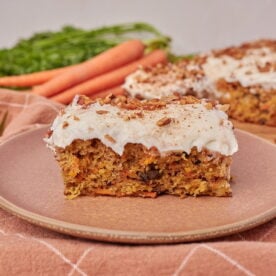 One slice of sourdough carrot cake with cream cheese frosting on a brown plate.