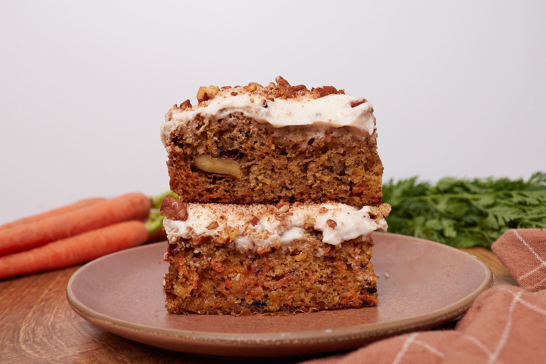 Two slices of Sourdough Carrot Cake stacked on top of each other on a brown plate.