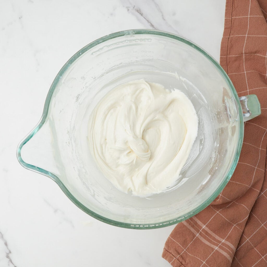 Cream cheese frosting for sourdough carrot cake mixed together in a clear bowl.