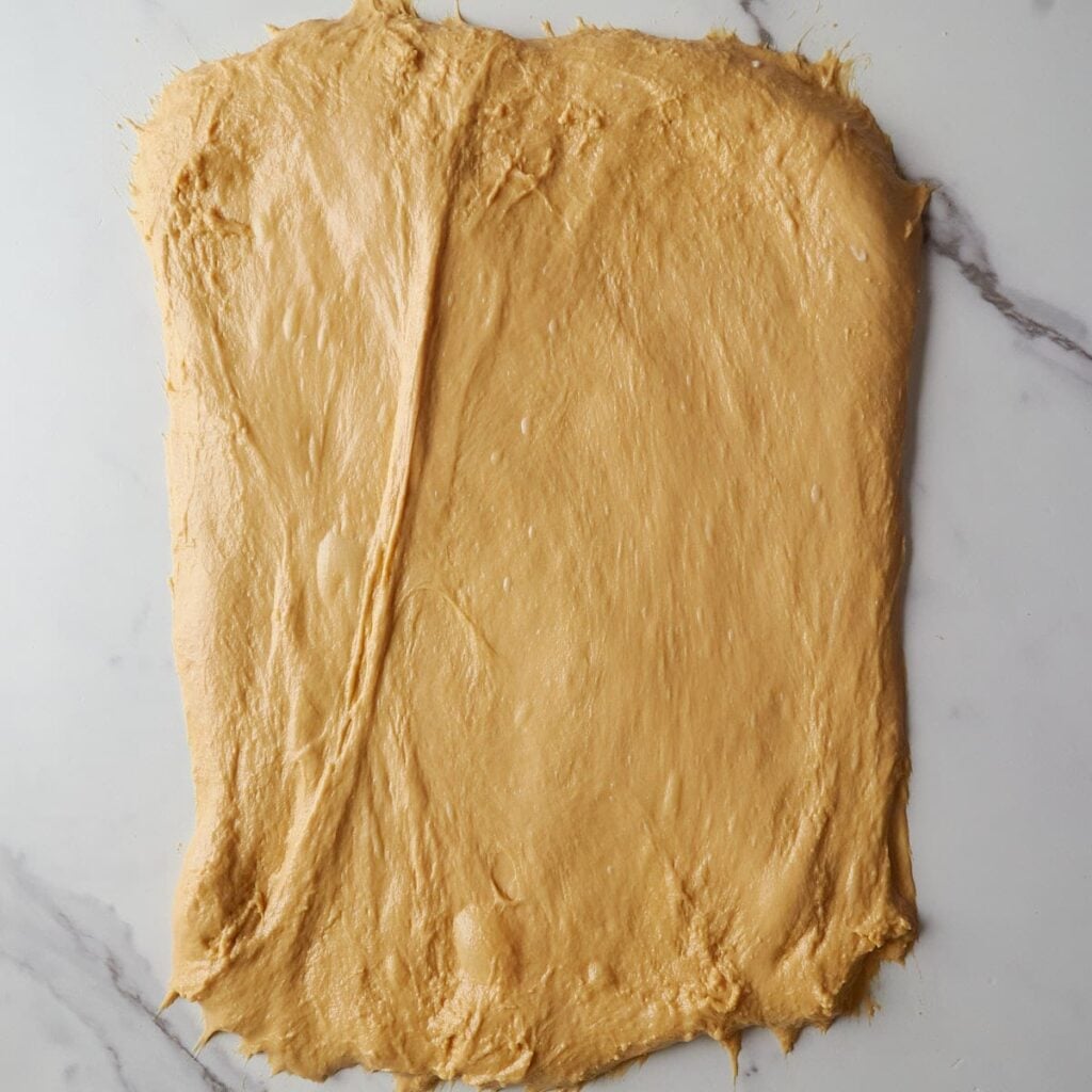 Dough stretched out into a chubby rectangle for lamination for carrot cake sourdough bread.