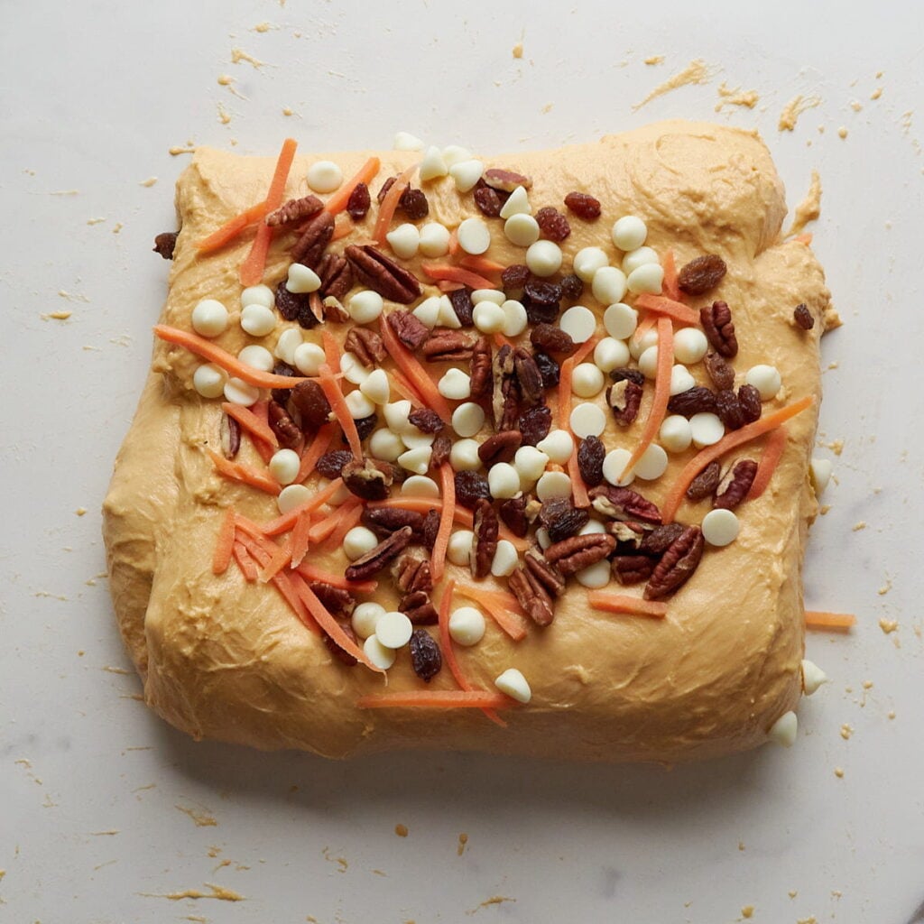 Final layer of shredded carrots, pecans, raisins and cream cheese chips added to dough during lamination.