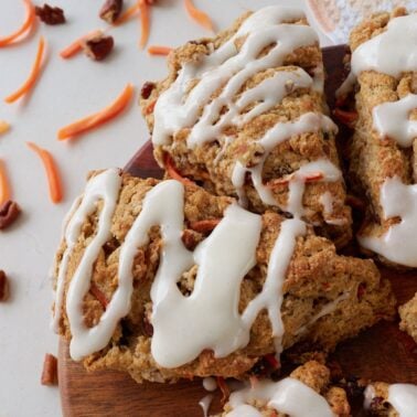 Sourdough easter recipe, carrot cake sourdough scones cut into wedges with cream cheese icing on top and shredded carrots and raisins around it.