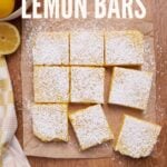 Sourdough Lemon Bar cut into squares on brown parchment paper next to lemons.