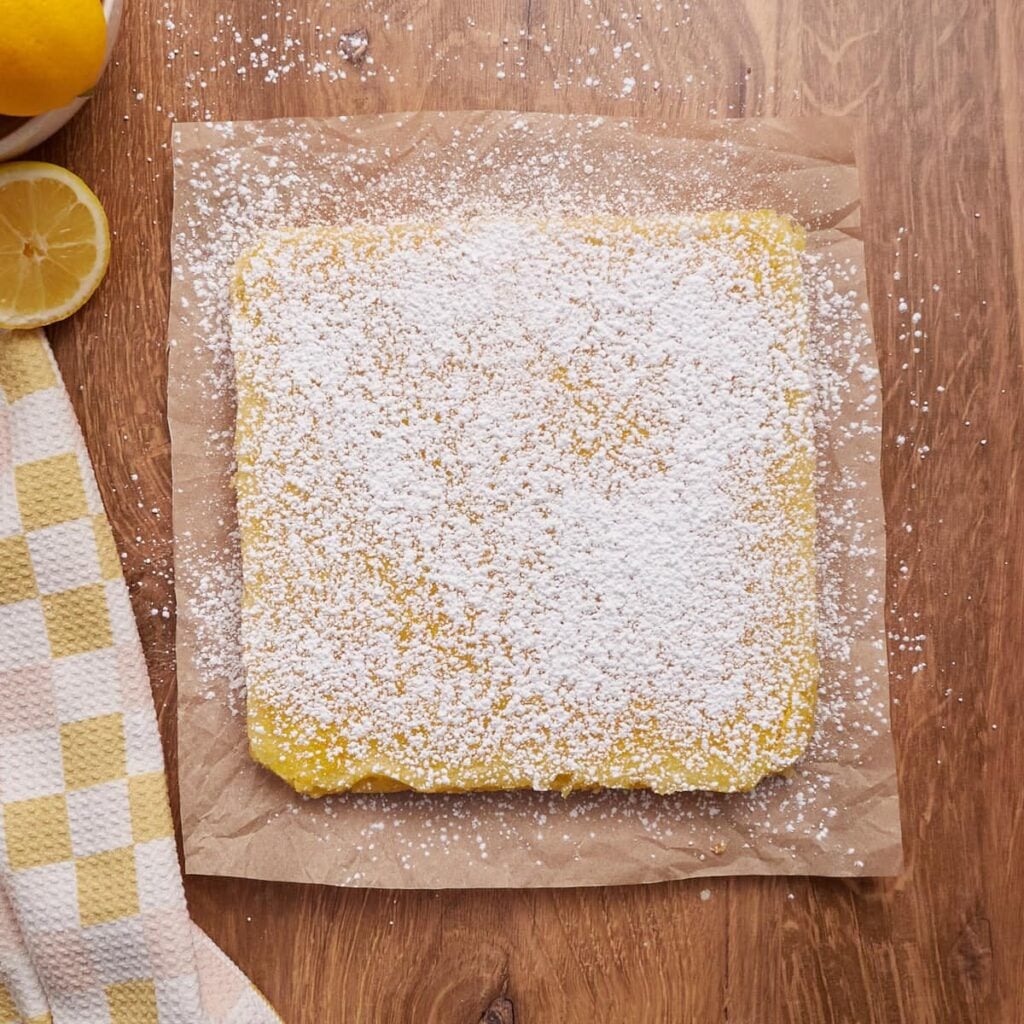Sourdough lemon bars on a piece of brown parchment paper with a dusting of powdered sugar.