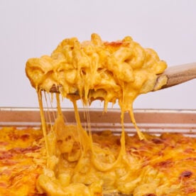 A wooden spoon taking a spoonful of sourdough mac and cheese out of a 9x13 pan filled with mac and cheese.
