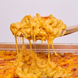 A wooden spoon taking a spoonful of sourdough mac and cheese out of a 9x13 pan filled with mac and cheese.