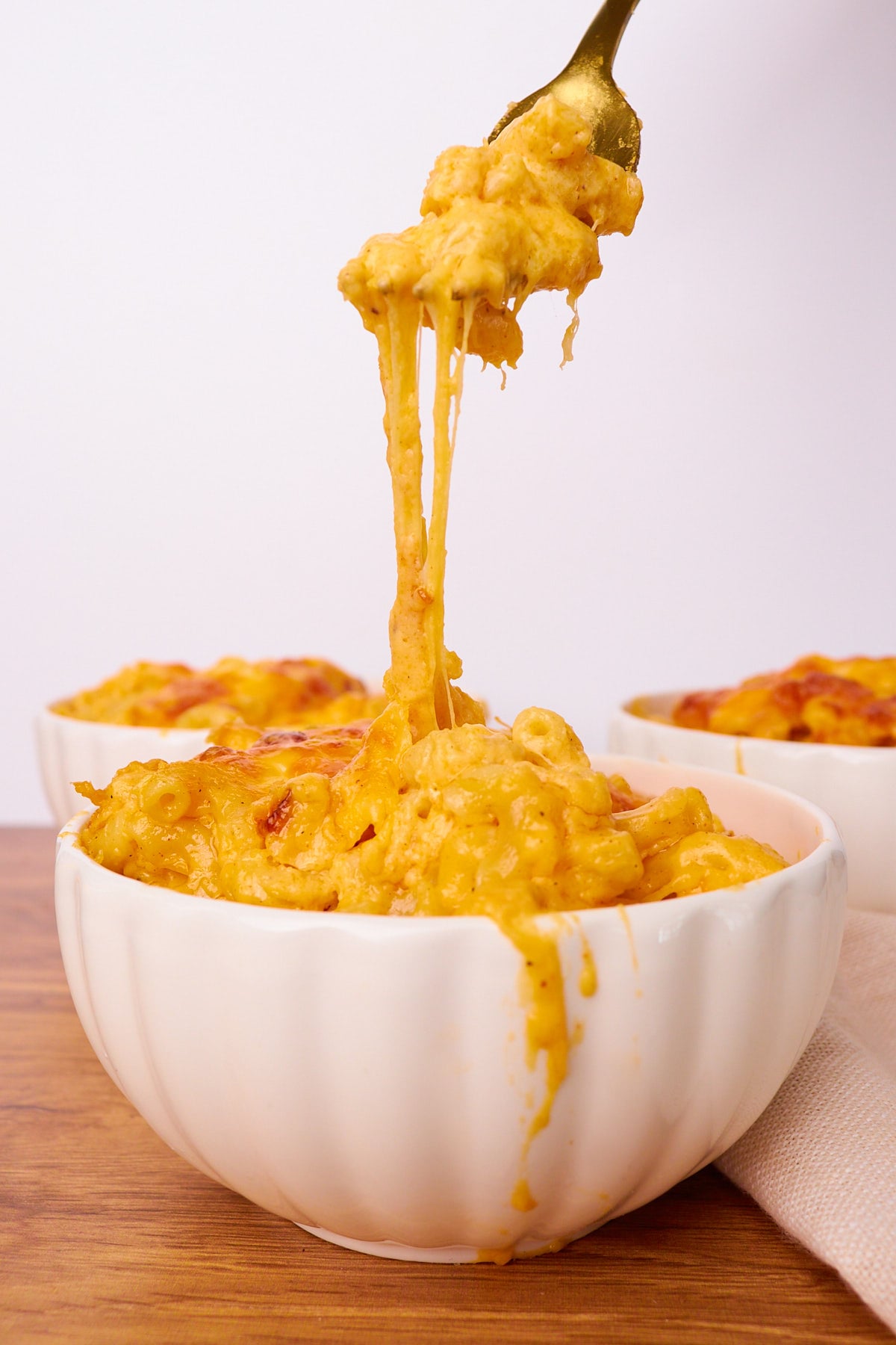 Three bowls of sourdough mac and cheese with a fork pulling some mac and cheese up with a cheese pull.
